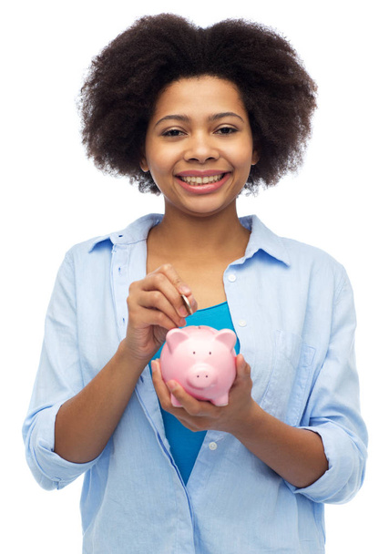 happy african woman putting coin into piggy bank - Foto, immagini