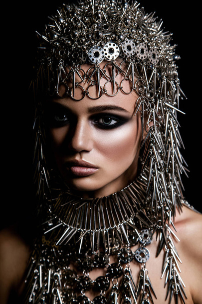High fashion beauty model with metallic headwear and dark makeup and blue eyes on black background - Fotó, kép