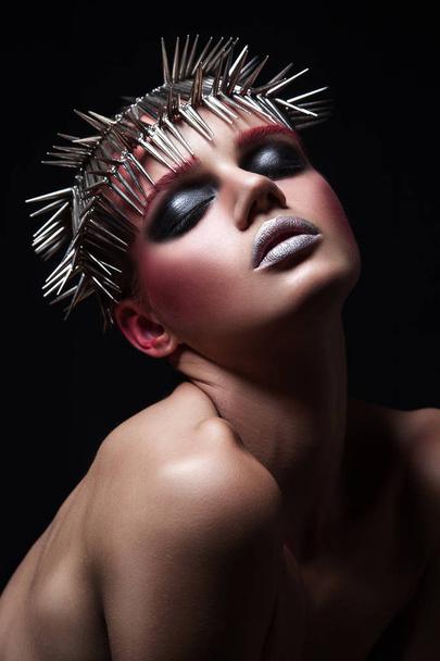 Мода модель красоты с металлической головной убор и блестящий серебристо-красный макияж и голубые глаза и красные брови на черном фоне
 - Фото, изображение