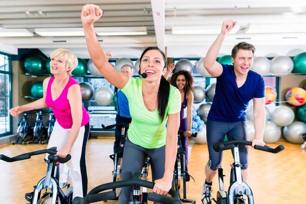 Grupo de homens e mulheres girando em bicicletas de fitness no ginásio
 - Foto, Imagem