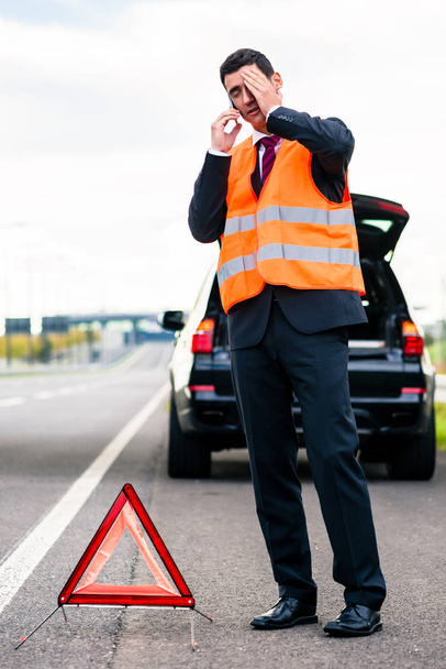 Hombre con avería de coche erigiendo triángulo de advertencia
 - Foto, imagen