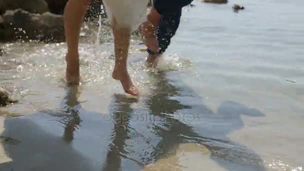 Legs of bride and groom runing barefooted in the water - Felvétel, videó