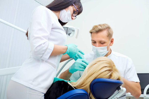 Dentist man with assistant treats teeth patient in hospital offi - Zdjęcie, obraz