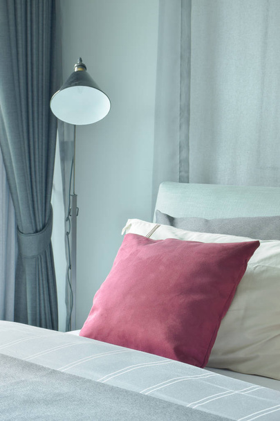 Red velvet pillow setting on bed with standing lamp next to bed - Foto, Imagem