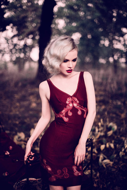schöne und elegante blonde Frau mit roten Lippen und Haaren Wellen tragen weinroten Nachthemd posiert auf dem Bett im Freien Herbst, Retro-Vintage-Stil und Mode. retuschierte Tonung Schuss - Foto, Bild
