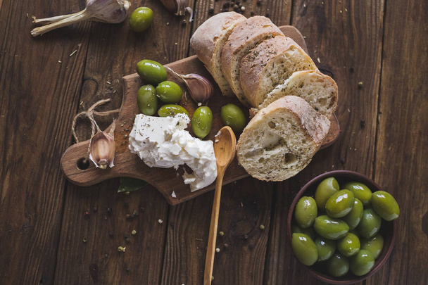 Green olives, sliced ciabatta, feta cheese on a wooden board. Spice. Garlic. Chees Feta. Ciabatta. Olives on a wooden background. Copyspace - Photo, image