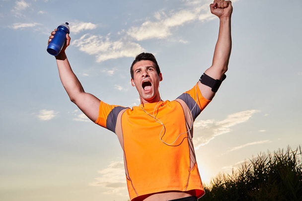 Successful man raising arms after cross country running on summer at sunset  - Photo, Image