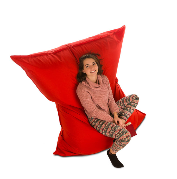 Attractive young woman sitting on red beanbag sofa chair for liv - Фото, изображение