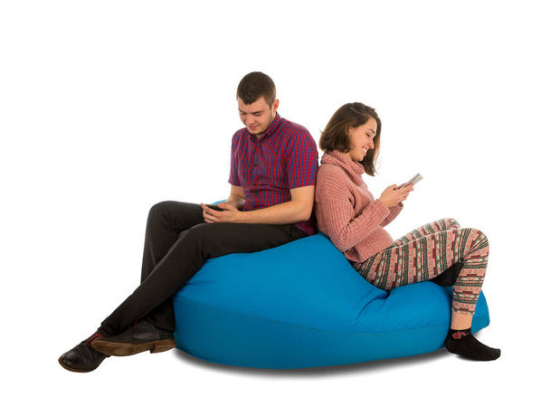 Young attractive man and woman sitting on blue beanbag sofa and  - Photo, Image