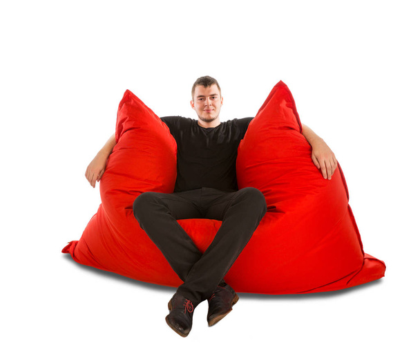 Young man sitting on big red beanbag sofa chair isolated on whit - Zdjęcie, obraz