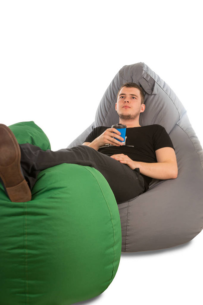 Young pensive man lying on beanbag chairs and holding coffee - Foto, Bild