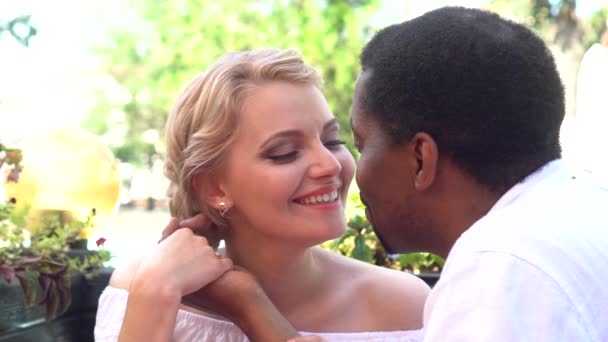 Ανάμικτο ζευγάρι φιλί σε μια καφετέρια στην καλοκαιρινή μέρα. Ευτυχισμένο ζευγάρι Αφρικανικός Αμερικανός διαφυλετικός σε μια ημερομηνία που είναι εξωτερική  - Πλάνα, βίντεο