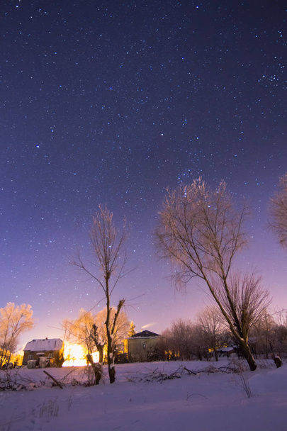 Cielo lleno de estrellas sobre el nevado pueblo de invierno
 - Foto, Imagen
