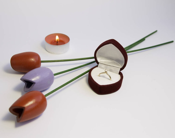 Caja de terciopelo rojo con anillo de compromiso, vela y flores en fondo blanco. Fondo del día de San Valentín
. - Foto, Imagen