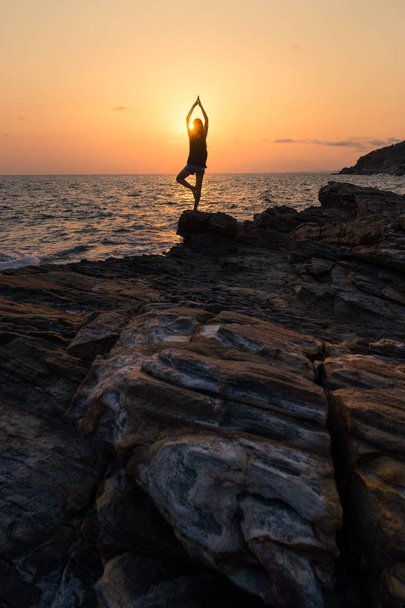Silhouette young woman practicing yoga on the rock at sunset, Ra - Photo, Image