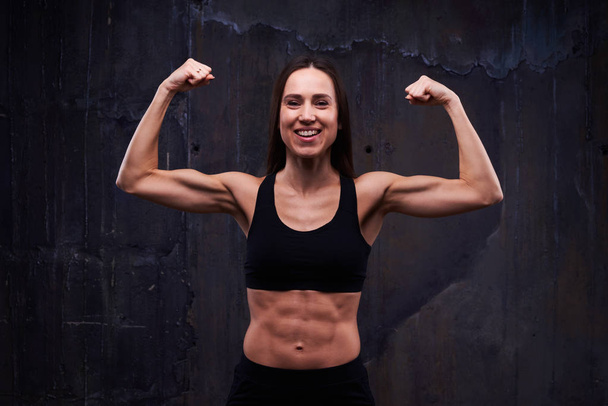 Modelo de fitness feliz mostrando bíceps entrenados aislados contra blac
 - Foto, imagen