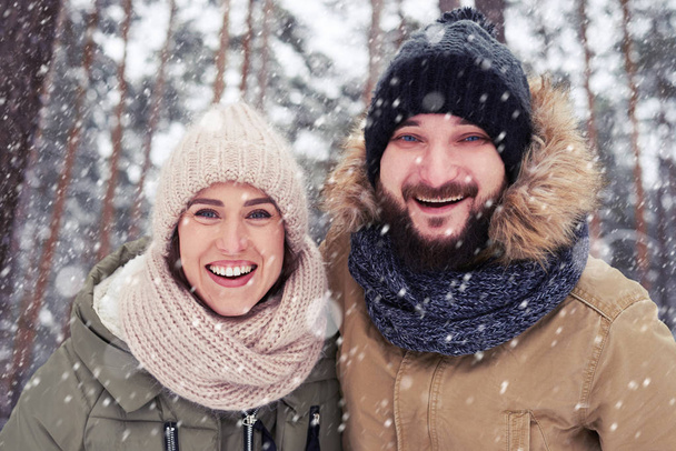 Vista de ángulo bajo de la pareja sonriente y abrazadora bajo el fal de nieve
 - Foto, Imagen