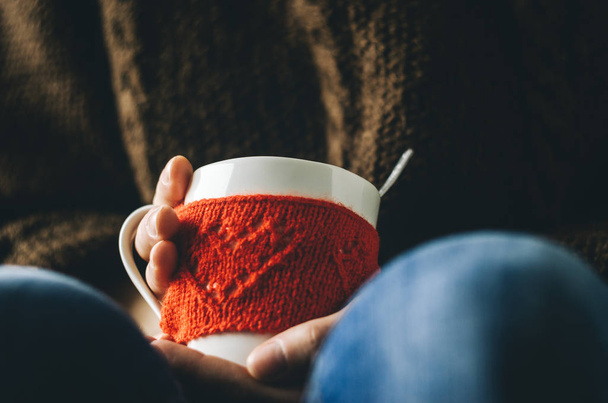 Red Knitted woolen cup with heart pattern in female hands. - Fotó, kép