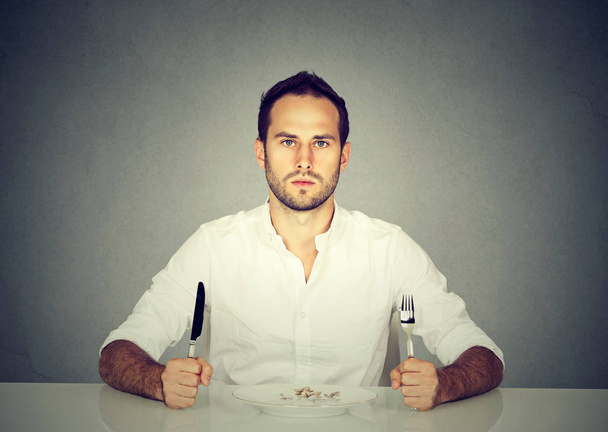 Homem com garfo e faca sentado à mesa com placa vazia
  - Foto, Imagem