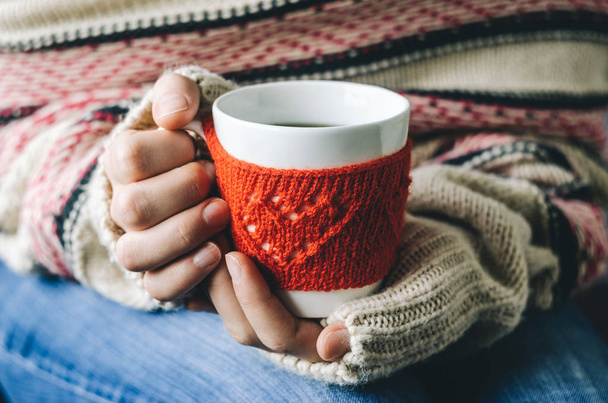 Red Knitted woolen cup with heart pattern in female hands. - Fotografie, Obrázek