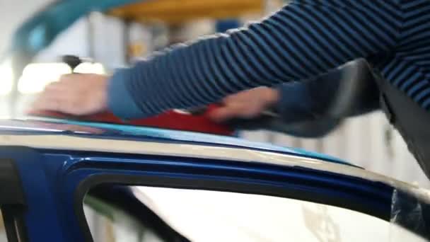 Αυτοκινητική υπηρεσία - ένας εργαζόμενος γυαλίζει ένα μπλε αυτοκίνητο, πλαϊνή όψη - Πλάνα, βίντεο