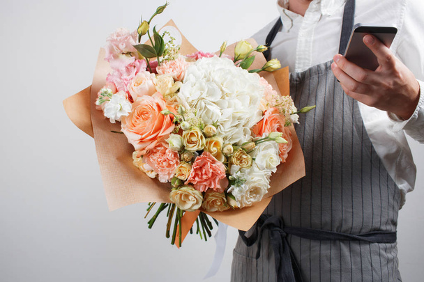 krásná kytice z různých květin v ruce mladého muže. pestré barvy mix květin. Pracovní oděvy v bílé košili a šedé zástěra - Fotografie, Obrázek