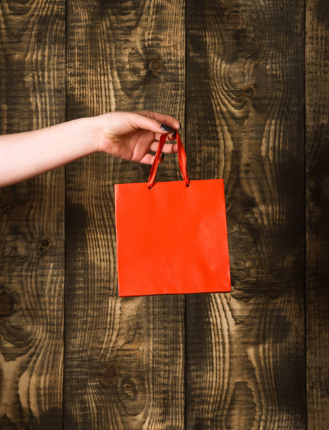 red orange shopping bag in female hand on wooden background - Photo, Image