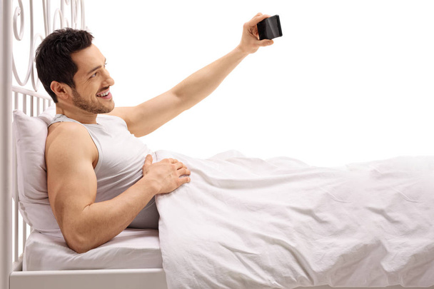 Άντρας ξαπλωμένος στο κρεβάτι και λαμβάνοντας μια selfie - Φωτογραφία, εικόνα