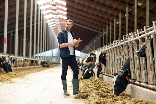 farmer with clipboard and cows in cowshed on farm - Foto, afbeelding