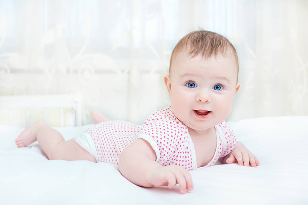 Cute baby smiling while lying on a white bed - Foto, afbeelding