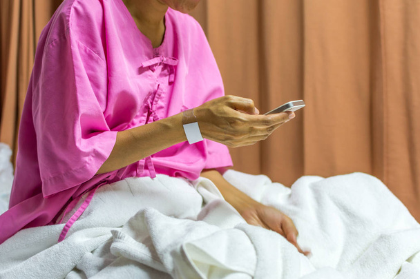 患者の女性がベッドの上にスマート フォンを使用して - 写真・画像