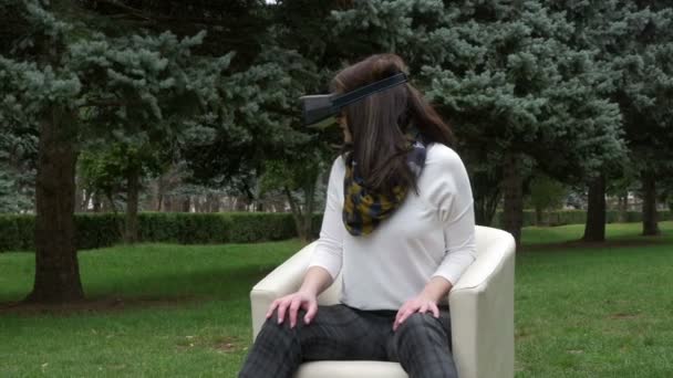 Young woman using virtual reality glasses in park looking around and dry leaves falling - Video