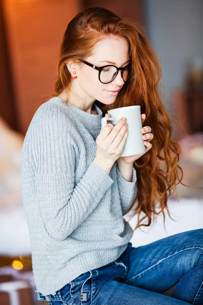 young red haired girl holding cup of tea sitting in Christmas decorated room - Foto, Imagem