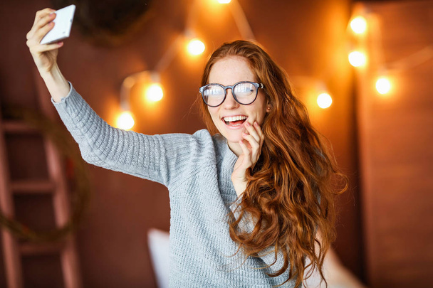 young beautiful girl holding eyeglasses sitting on bed in Christmas decorated room  - Fotoğraf, Görsel