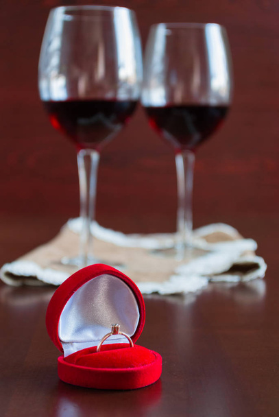 Dos copas de vino sobre una mesa de madera. Caja roja con anillo de compromiso
 - Foto, imagen