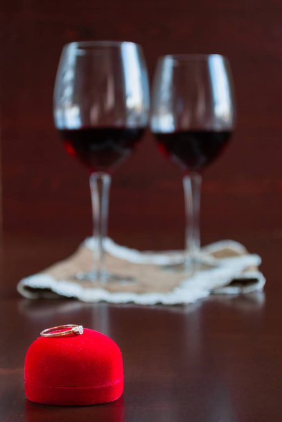Two glasses of wine on a wooden table. Red box with engagement ring - Fotoğraf, Görsel