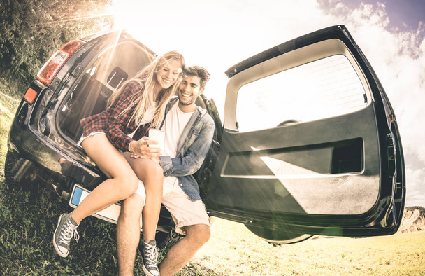 junges glückliches Paar, das im Moment der Autofahrt Spaß mit dem Handy hat - Fernweh-Konzept während des glücklichen Reiseurlaubs unterwegs - entsättigter Vintage-Kontrastfilter mit Schwerpunkt Gesichter - Foto, Bild