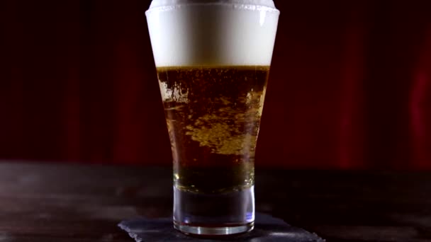 Szklanka do piwa z bąbelkami dzieje na drewnianym stole - Materiał filmowy, wideo