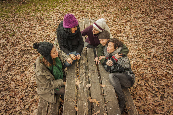 Friends talking in a bench in a park in autumn - Фото, изображение