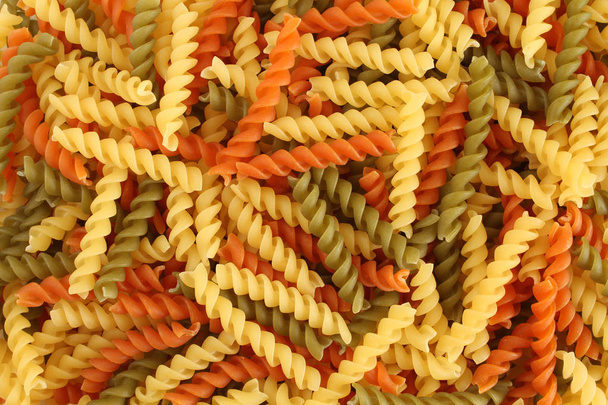 Food background - uncooked three-colored Fusilli durum wheat pasta with spinach and tomato - Photo, Image
