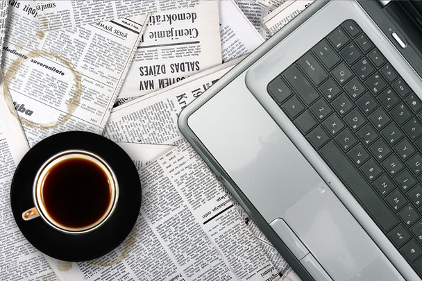 Рабочее место с ноутбуком и кофейной чашкой на фоне газеты
 - Фото, изображение