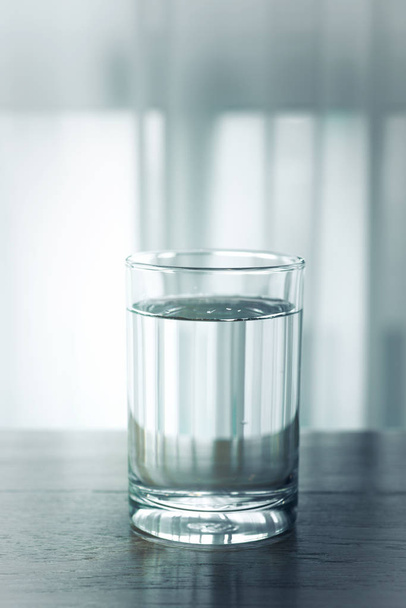 Glass of water on wooden table and light blurred background. - Valokuva, kuva