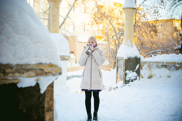young woman dressed in warm clothes drinking takeaway coffee from the cup on the street in winter - Foto, imagen