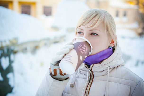 young woman dressed in warm clothes drinking takeaway coffee from the cup on the street in winter - Fotografie, Obrázek