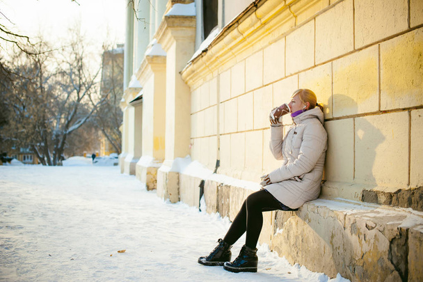 young woman dressed in warm clothes drinking takeaway coffee from the cup on the street in winter - Valokuva, kuva