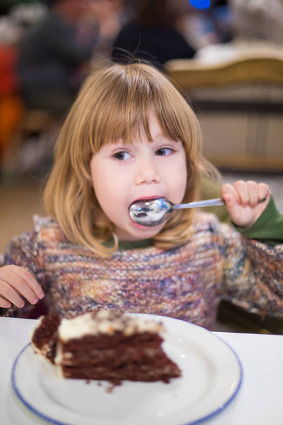 little child licking spoon with chocolate cake at restaurant - Photo, Image