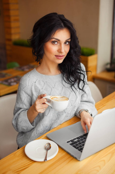 woman sitting at a laptop and drink coffee - Φωτογραφία, εικόνα