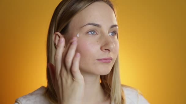 Female beauty, happy mid adult woman putting cream on face skin and smiling, looking at camera. - Imágenes, Vídeo