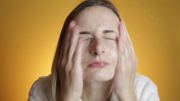 Blonde woman splashing her face against a on a yellow background - Кадри, відео