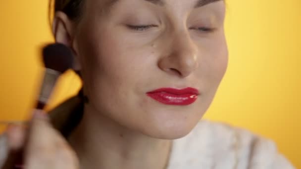 Beautiful happy young lady putting makeup on a yellow background - Záběry, video